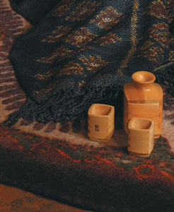 
Atop a wool rug blending the colors of the sky, the earth, and the greenery of Peru, a sueng klang, a four-stringed strumming instrument used in festivals and ceremonies in northern Thailand, rests against a teak and rattan bench made by Balinese artist Wayan Pastika (all from Novica.com). Cushioning the sueng is a naturally dyed kid-mohair throw from New Zealand (womankind.com). The walls are adorned with a Zimbabwean potato print wall hanging, a Balinese mahogany relief panel depicting the interaction of flora and fauna, and a hibiscus and batik mask (all from Novica.com). Cornhusk flowers handmade in Honduras (available from aid2artisans.org) and safari candles from Zimbabwe (Novica.com) complete this exotic room.
